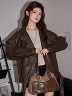 Woman holding a brown handbag while wearing a brown faux leather moto jacket and grey crop top.