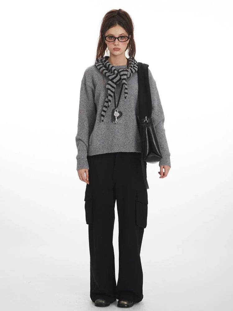 Woman wearing a grey knit sweater with a striped scarf and black cargo pants, front view. Main image