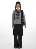Woman wearing a grey knit sweater with a striped scarf and black cargo pants, front view.