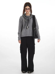 Woman wearing a grey knit sweater with a striped scarf and black cargo pants, front view.