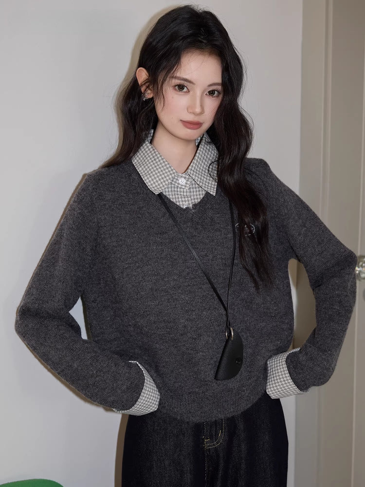 Woman standing with hands on hips, wearing a grey v-neck sweater over a checkered collared shirt, dark wash wide leg jeans, and a black crossbody pouch.