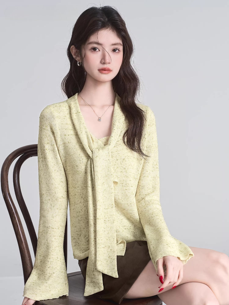 Woman sitting on a chair, wearing a light yellow textured knit top with a draped neckline and scarf tie.