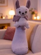 A person's leg wearing a light purple ankle sock with a plush bat character attached to the cuff, standing on a rug.