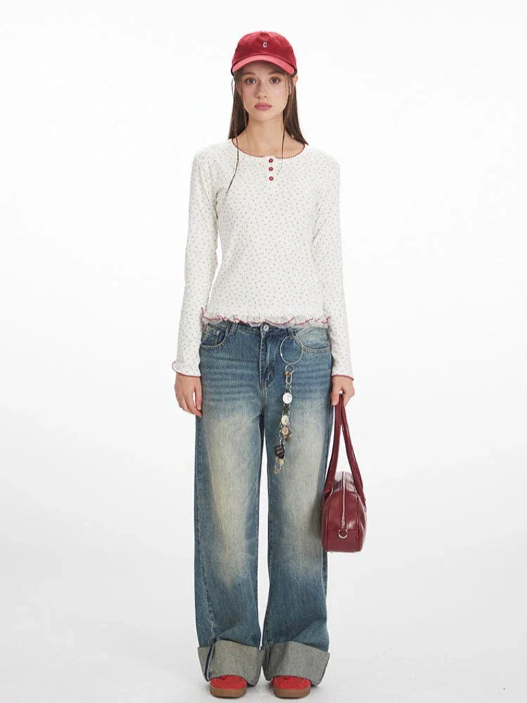Model wearing a white long-sleeve top with a floral print and red trim, paired with blue jeans and a red baseball cap.