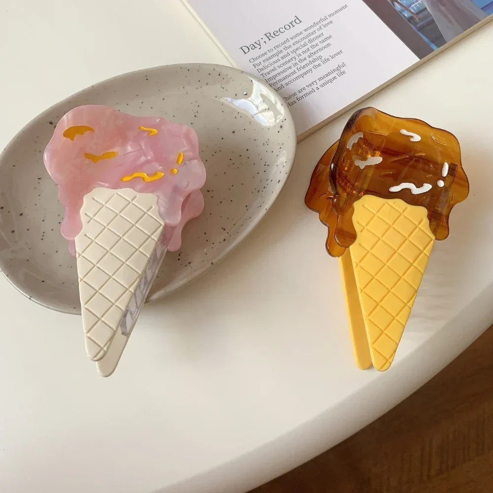 Two ice cream cone hair clips, one pink and one brown, on a textured plate and a white surface