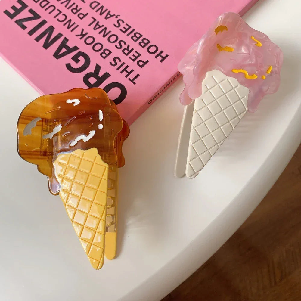 Two ice cream cone hair clips, one pink and one brown, on a white surface with a pink book in the background