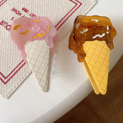 Two ice cream cone hair clips, one pink and one brown, on a textured placemat