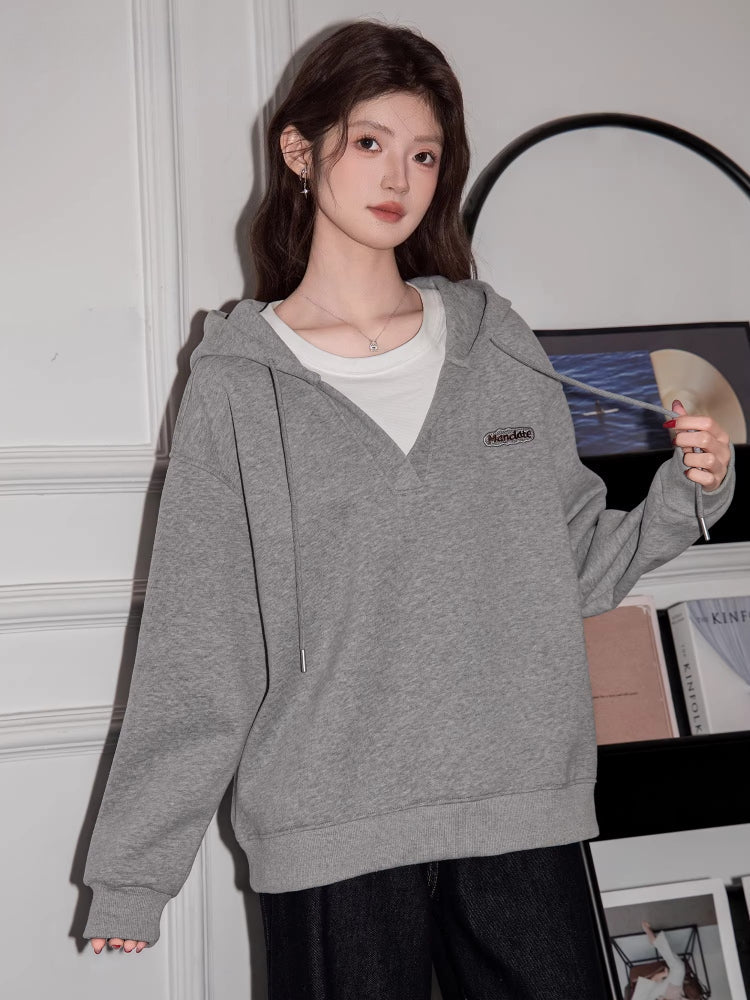 Woman wearing a grey V-neck oversized hoodie and black jeans, holding a blue tote bag.