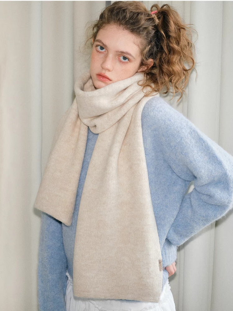 Model wearing a light blue knit sweater and a cream scarf, with one hand on hip.