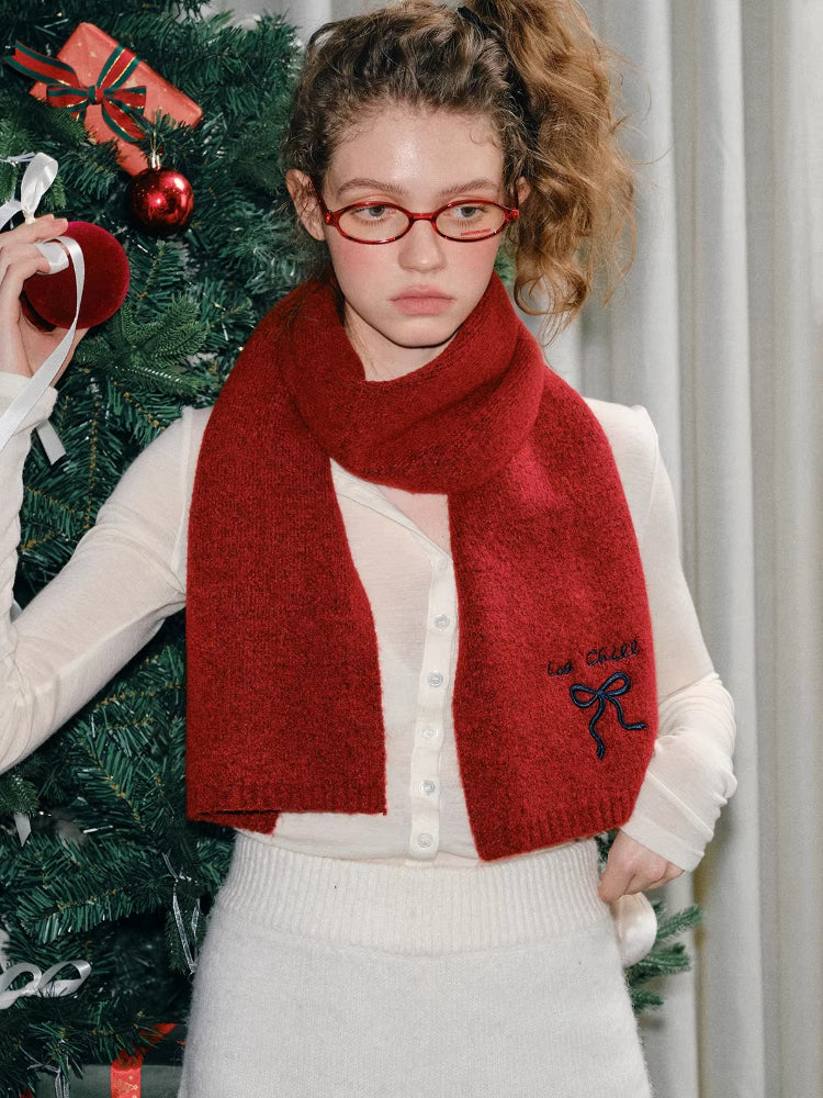 Woman in a red knit scarf with embroidered details, posing by a Christmas tree.