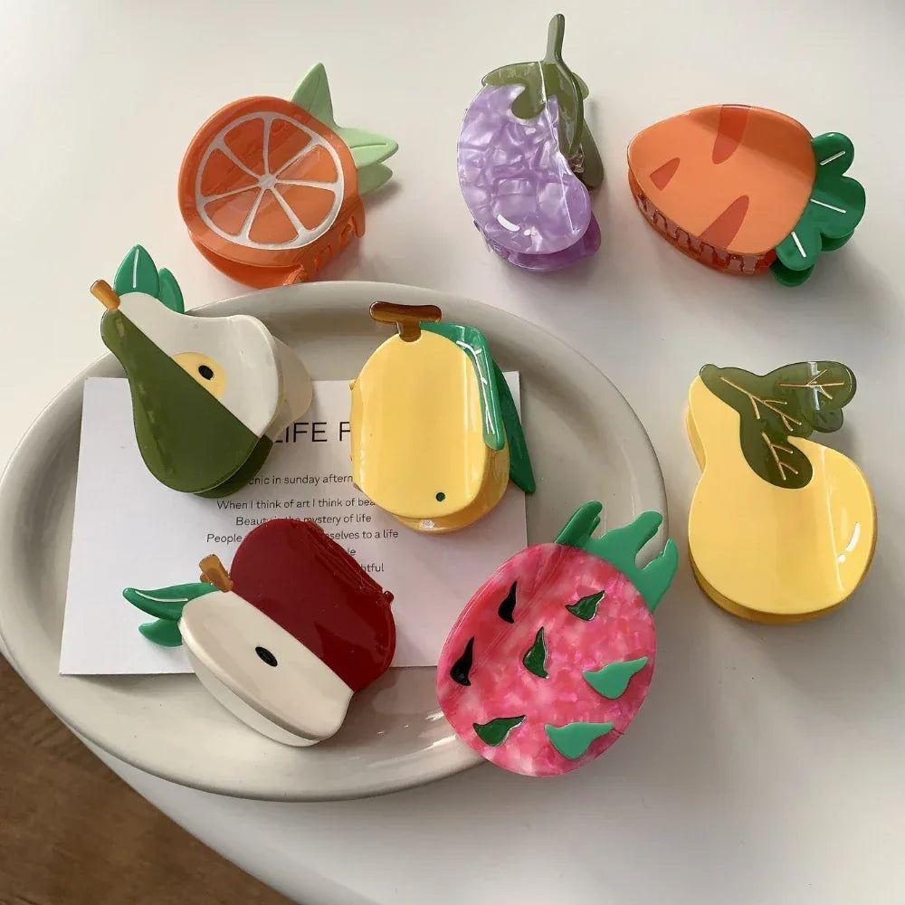 Arrangement of fruit-shaped hair claw clips on a white plate with a piece of paper showing text