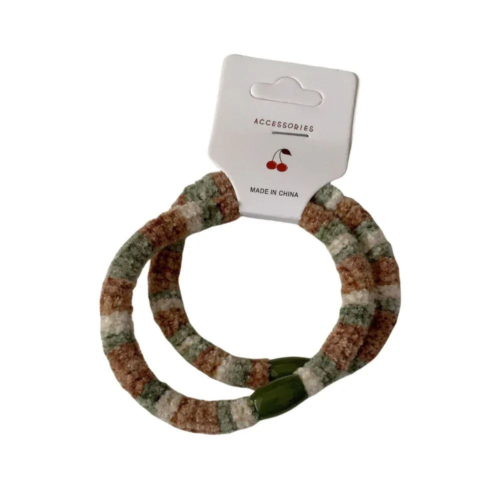 A pair of fuzzy striped hair ties with green beaded accents, attached to a white accessory tag. Main image