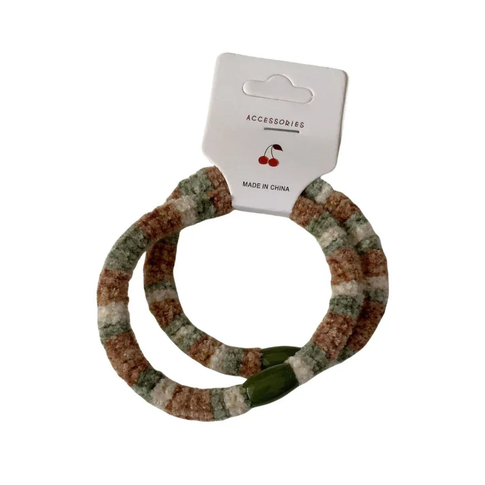 A pair of fuzzy striped hair ties with green beaded accents, attached to a white accessory tag. Main image