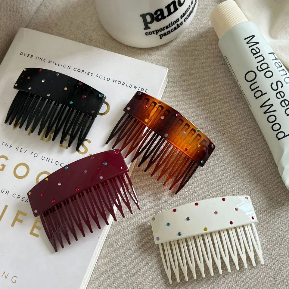 Four hair combs in different colors (black, tortoiseshell, burgundy, and white) arranged on a book and fabric. Secondary image