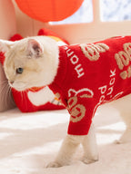 A white cat walking, wearing a red knit sweater with gold Chinese character designs.