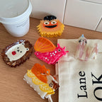 A group of decorative hair clips including a fox, hedgehog, snail, seal, and a fuzzy character, placed near a coffee cup and a canvas bag.