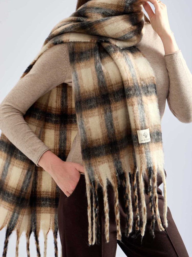 Woman with an oversized plaid scarf around her neck, one hand in her pocket, looking to the side.