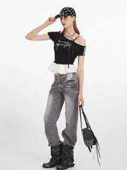 Full body shot of a woman wearing a black off-the-shoulder top with white ruffle trim, grey jeans, and black boots.