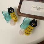 Two bee-shaped hair clips with blue wings, resting on a white surface next to a wooden tray.