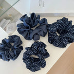 An overhead view of four scrunchies, two polka dot and two denim, arranged on a white surface with books in the background