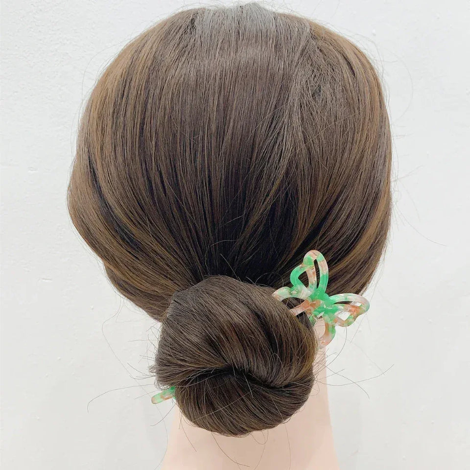 woman with brown hair in a bun wearing a green and orange butterfly hair stick Secondary image