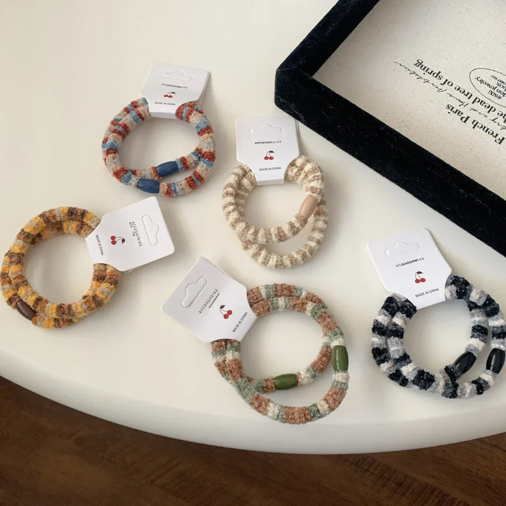 A collection of fuzzy striped hair ties in various color patterns, displayed on a white surface.