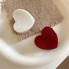 White and red heart-shaped hair clips on a burlap square