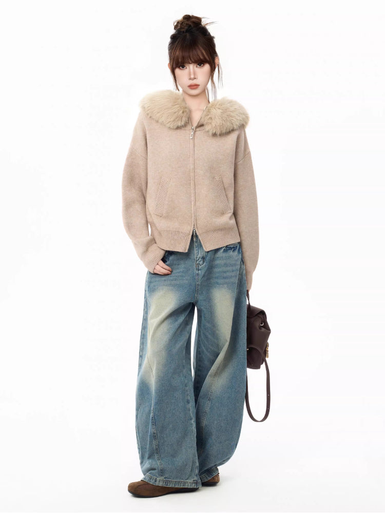 Full body shot of a woman wearing a beige knit cardigan with a faux fur collar and wide-leg blue jeans, holding a brown backpack