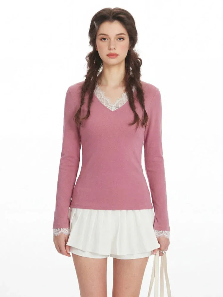 Woman wearing a pink long-sleeved top with white lace trim at the neckline and cuffs, and white pleated shorts.