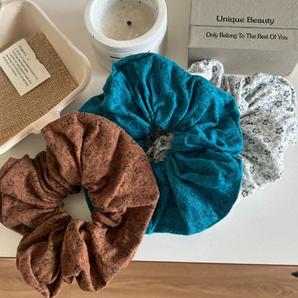 three scrunchies in teal, white with floral pattern, and brown arranged on a white surface