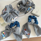 Assortment of black and white gingham scrunchies with denim bows and dog appliques on a white surface