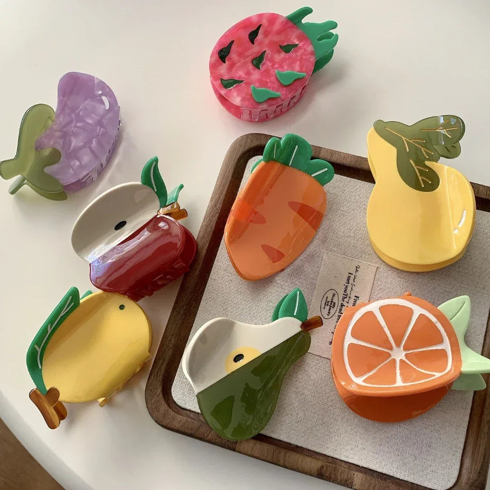 Collection of fruit-shaped hair claw clips including a dragon fruit, carrot, pear, orange slice, apple, lemon, and eggplant