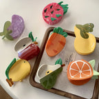 Collection of fruit-shaped hair claw clips including a dragon fruit, carrot, pear, orange slice, apple, lemon, and eggplant