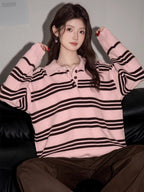 Woman wearing a pink and black striped knit polo sweater and brown pants, sitting on a black couch.
