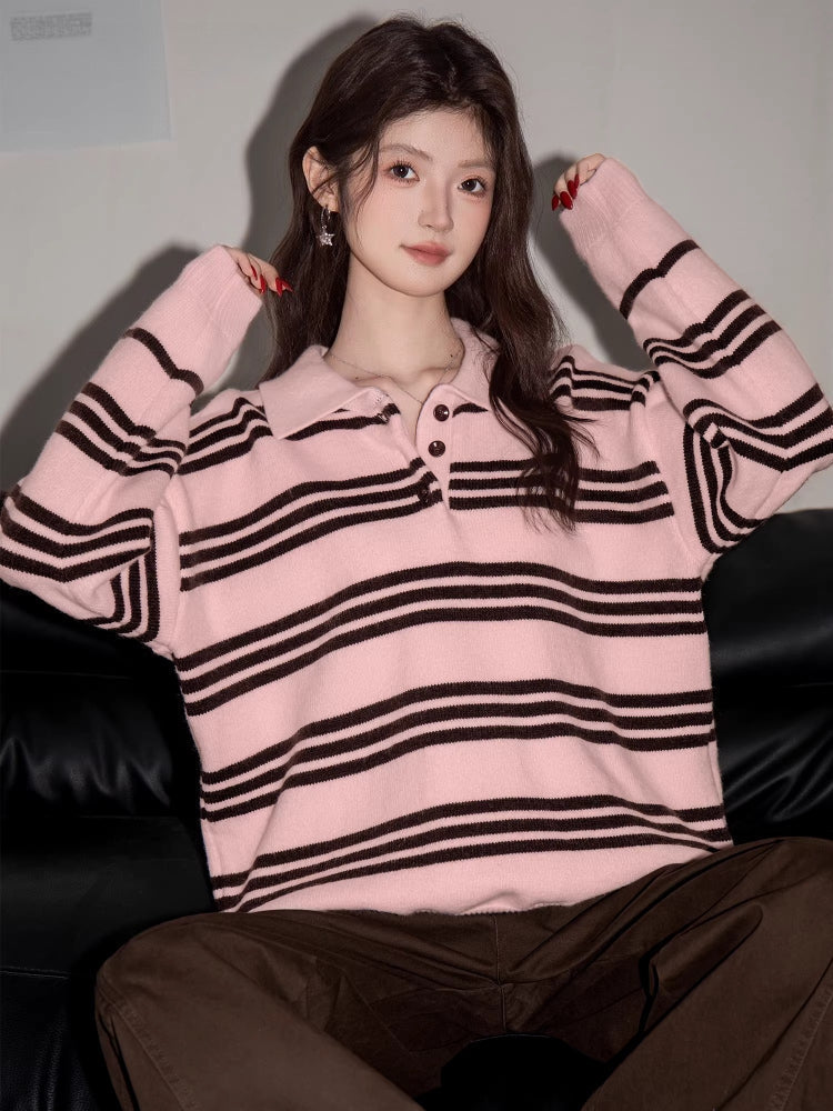 Woman wearing a pink and black striped knit polo sweater and brown pants, sitting on a black couch.