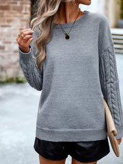 Woman wearing a grey knit sweater with cable knit sleeves and black shorts, holding a beige clutch.