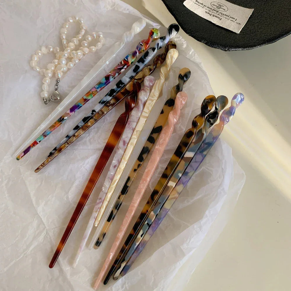A collection of patterned hair sticks laid out on white paper, with a pearl necklace and a black dish.