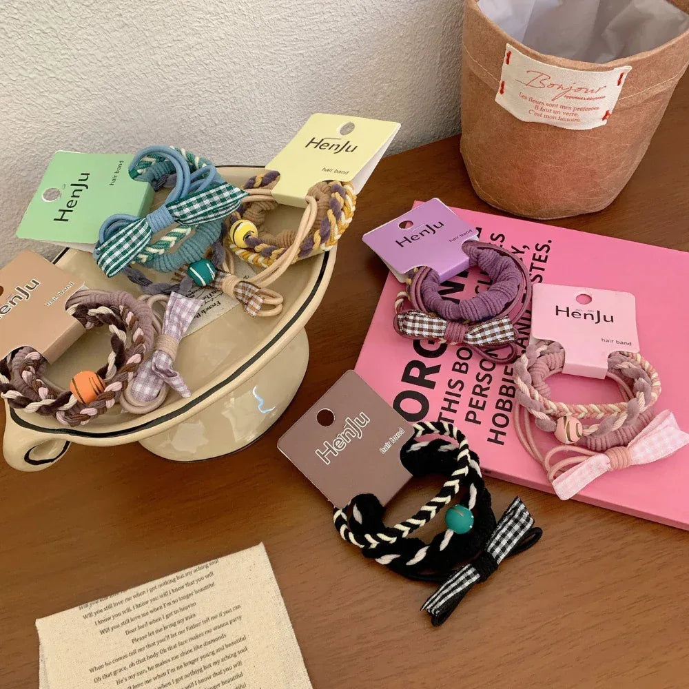 A variety of hair ties with plaid bows and braided designs are displayed on a table with other decorative items.
