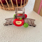 A detailed view of a transparent hair claw clip featuring a red apple charm and green beads, on a textured surface.