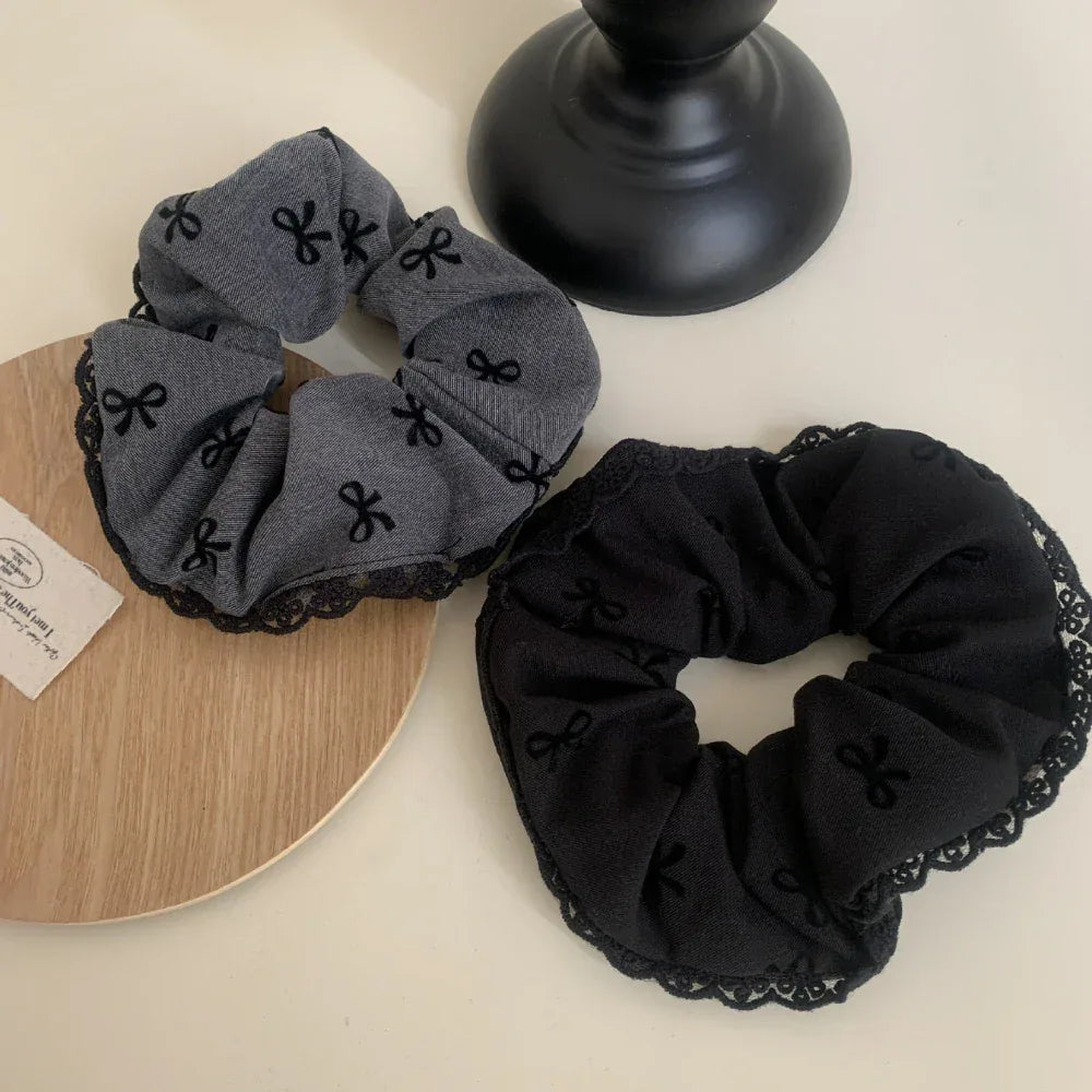two scrunchies, one grey and one black, with bow patterns and lace trim