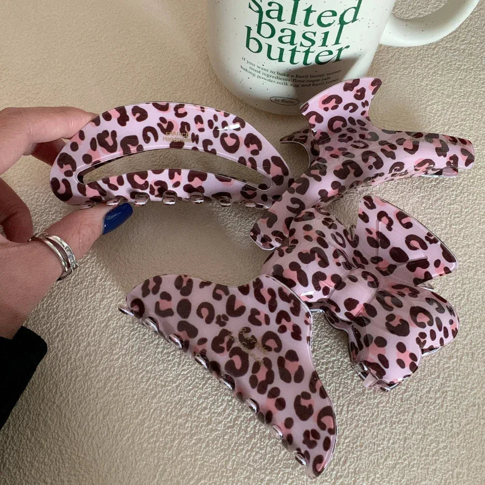 hand holding a pink leopard print hair claw clip with other clips nearby