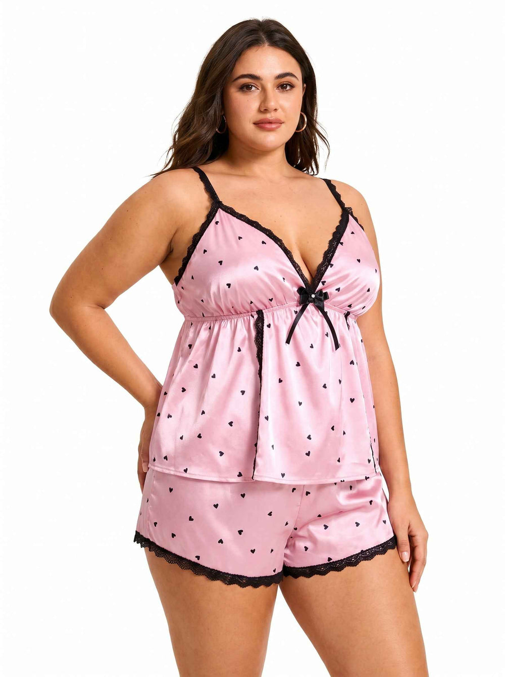 Side front view of a pink satin cami and shorts pajama set with black heart print and lace trim.