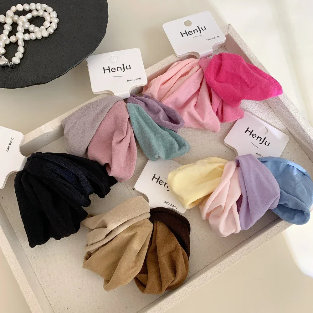 A collection of scrunchie sets in various colors, such as pink, purple, blue, yellow, brown, and black, arranged on a tray.