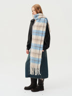 Side view of a model wearing a black jacket, grey top, denim skirt, and a long blue and beige plaid scarf with fringe