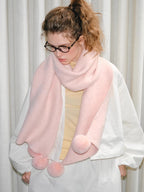 Woman wearing a pink fuzzy knit scarf with pom-pom embellishments, looking down.