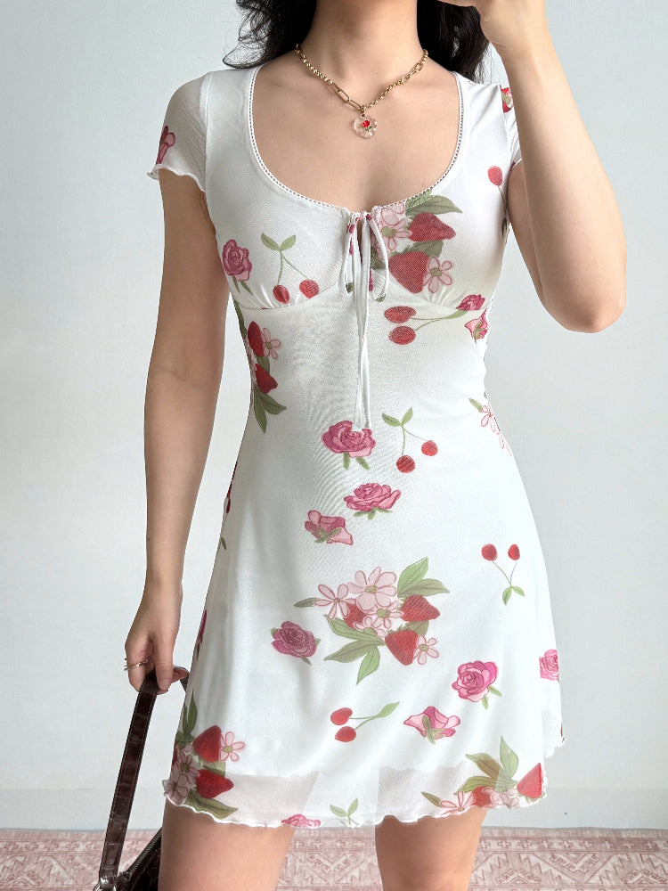 Side view of a woman wearing a white short-sleeve dress with a strawberry and rose print and a sheer hem.