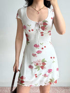 Side view of a woman wearing a white short-sleeve dress with a strawberry and rose print and a sheer hem.