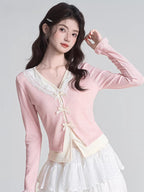 Woman adjusting her sleeve while wearing a pink V-neck knit cardigan with lace trim and bow closures.