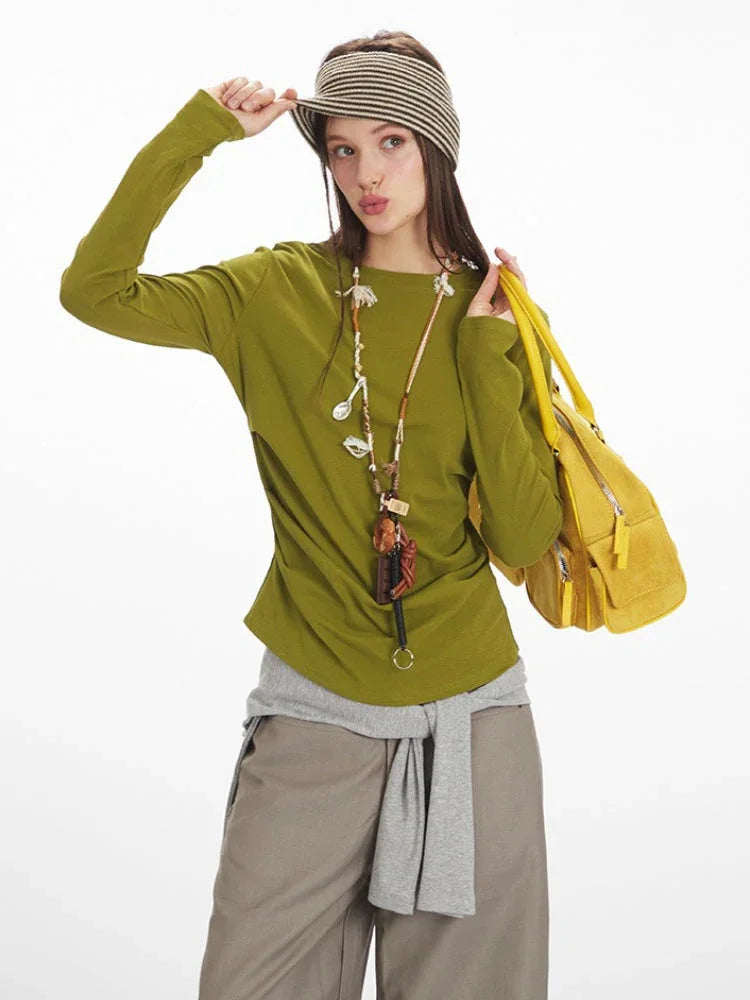 Woman wearing a green long-sleeved top, taupe wide-leg pants, and yellow handbag, adjusting her striped headband.