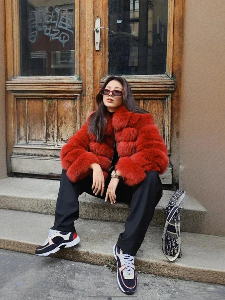 Woman wearing a red fur jacket and black pants sitting on steps Main image